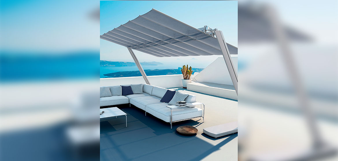 Outdoor rooftop patio in contemporary home, with concrete decking, white stucco half-walls overlooking an amazing seascape, chrome metal patio sofa with white cushions and matching coffee table, shaded by a FIM Manufacturing Flexy Zel FLEXY-ZEN commercial dual-post umbrella