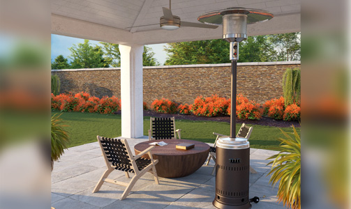 Outdoor patio with stone floor, maple wood chairs with black woven mesh seating and backs, wood bowl-shaped table, Fire Sense 63715 liquid propane patio heater in hammered bronze color, white pillars, and white ceiling with a background of lush lawn, flowering bushes, and large brick wall
