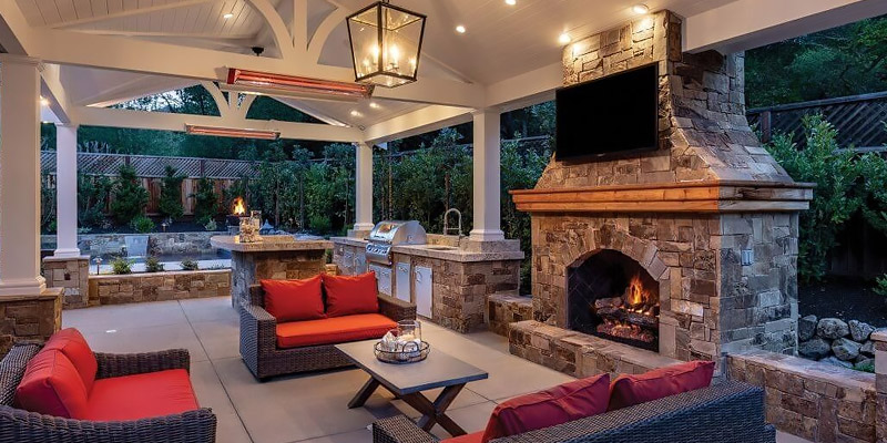 a covered outdoor living area with matching conversation set, coffee table, fireplace, and drop in grill lit with an outdoor chandelier and heated by ceiling-mount heaters
