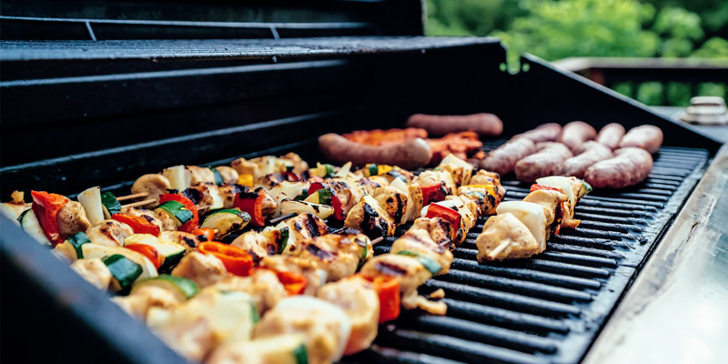 an outdoor living area featuring a a grill with vegetable and chicken kebabs and hotdogs