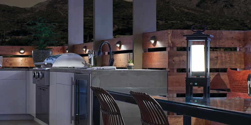 an outdoor living area with a drop in grill, deck lights, and a portable led lantern at night