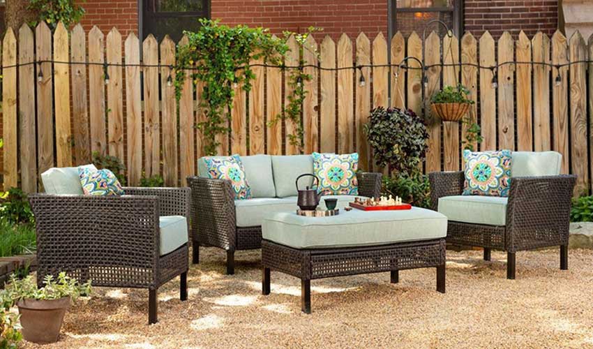 small patio furniture that looks like wicker and has blue cushions sitting on top of crushed gravel