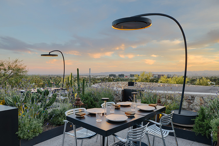 a freestanding  bromic eclipse heater with integrated light heating a modern patio table surrounded by desert plants