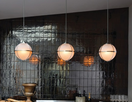 three lit kitchen pendants in front of a black tile wall